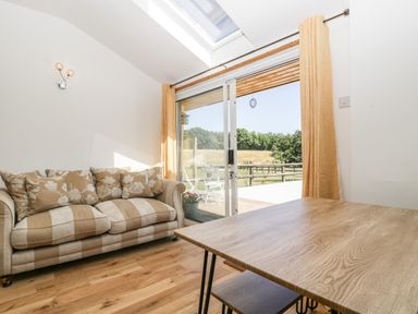A room with a striped sofa wooden table sliding glass doors with yellow curtains and a view of a patio and field at Steel Works Farm in Gorsley