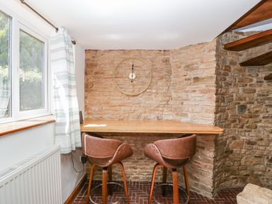 A corner seating area with two brown chairs and a wooden table against a stone wall with a clock near a window with striped curtains at Steel Works Farm in Gorsley