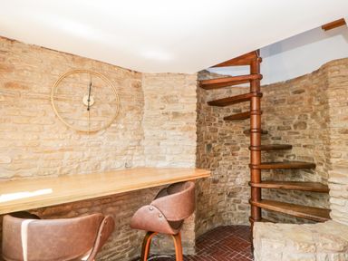 A corner with a wooden spiral staircase leather chairs and a wooden counter against a stone wall at Steel Works Farm in Gorsley