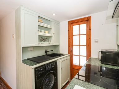 A kitchen with a black washing machine under a sink wooden cabinets a glass door and a black microwave on a countertop at Steel Works Farm in Gorsley