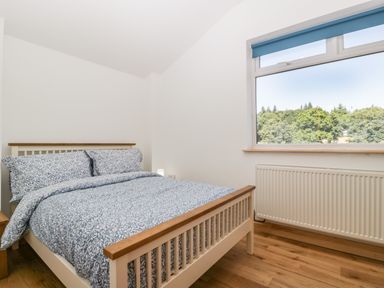 A bedroom with a wooden bed with floral bedding next to a window with a blue blind at Steel Works Farm in Gorsley