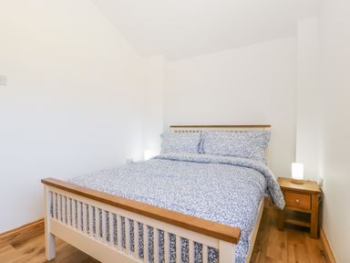 A bedroom with a bed with patterned blue and white bedding and a wooden nightstand with a lamp at Steel Works Farm in Gorsley