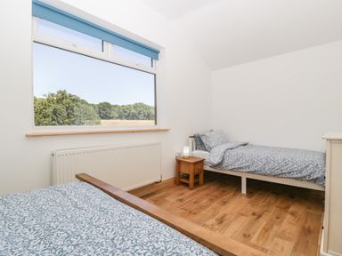 A bedroom with two single beds a wooden nightstand and a large window showing trees at Steel Works Farm in Gorsley