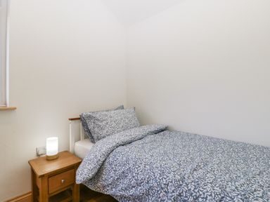 A small bedroom with a single bed with patterned bedding and a wooden bedside table with a lamp at Steel Works Farm in Gorsley