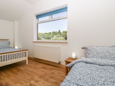 A bedroom with two beds, wooden flooring, a window with a blue blind, and a bedside table with a lamp at Steel Works Farm in Gorsley