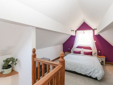 A bedroom with a double bed purple accent wall and wooden stair railing at Steel Works Farm in Gorsley