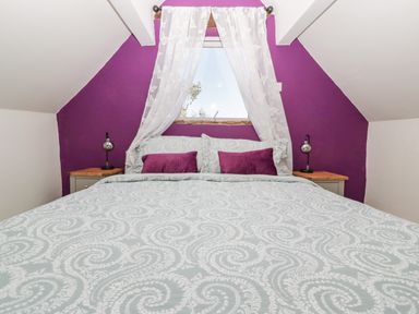 A bedroom with a bed covered in patterned bedding two side tables and a small window with curtains at Steel Works Farm in Gorsley