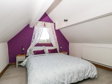 A bedroom with a bed and bedside tables under a window with white curtains at Steel Works Farm in Gorsley