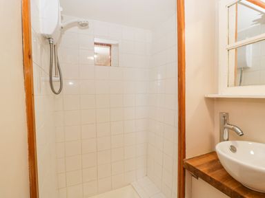 A tiled shower area with a showerhead and a sink with a faucet on a wooden countertop at Steel Works Farm in Gorsley