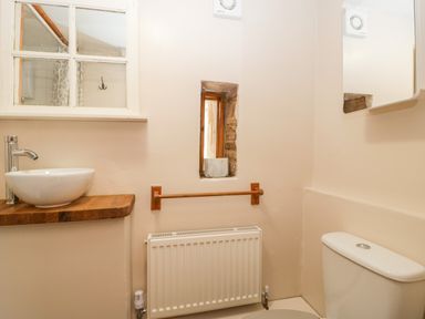 A bathroom with a sink on a wooden countertop a toilet radiator and a small window at Steel Works Farm in Gorsley