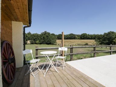 A wooden patio with two white metal chairs and a round table overlooking a fenced green field at Steel Works Farm in Gorsley