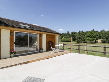 An outdoor patio with a small white table and two chairs next to a sliding glass door and a wooden fence overlooking a grassy field at Steel Works Farm in Gorsley
