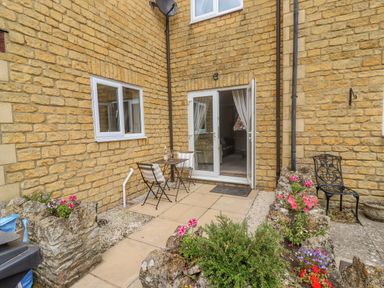 A small outdoor patio with a table and two chairs flowers in stone planters and a metal chair at The Cornerstone in Bourton-On-The-Water