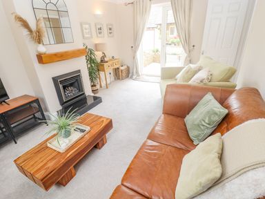 A living room with leather and fabric sofas a wooden coffee table a fireplace and glass doors at The Cornerstone in Bourton-On-The-Water