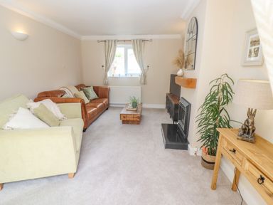 A living room with a green sofa and a brown leather sofa a wooden coffee table and a plant near a fireplace at The Cornerstone in Bourton-On-The-Water