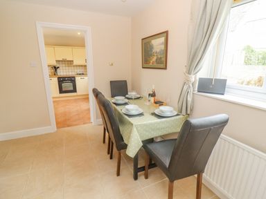 A dining area with a table set for four and a view into a kitchen at The Cornerstone in Bourton-On-The-Water