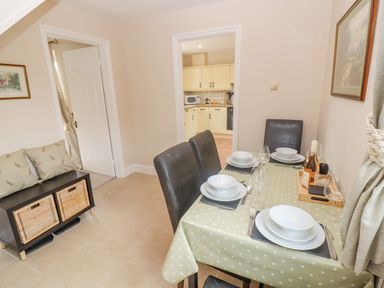 A dining area with a table set for four with a polka dot tablecloth and a small storage bench with cushions at The Cornerstone in Bourton-On-The-Water