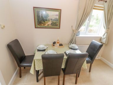 A dining area with a table set for four and four chairs near a window with curtains at The Cornerstone in Bourton-On-The-Water