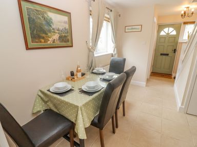 A dining table set for four with a green polka dot tablecloth and black chairs near a window and an entrance door at The Cornerstone in Bourton-On-The-Water