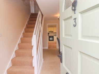 An open front door showing a hallway with carpeted stairs on the left and a kitchen at the end at The Cornerstone in Bourton-On-The-Water