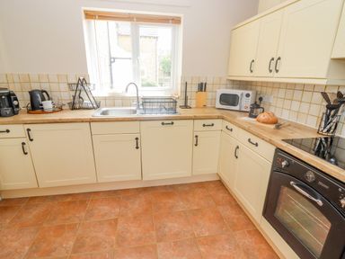 A kitchen with cream cabinets wooden countertops a sink a microwave oven and various kitchen appliances at The Cornerstone in Bourton-On-The-Water