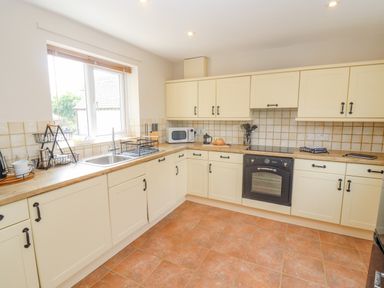 A kitchen with cream cabinets a tiled floor a window over the sink and various appliances on the counters at The Cornerstone in Bourton-On-The-Water