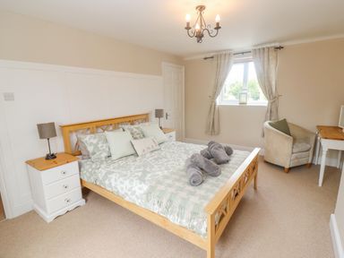 A bedroom with a wooden bed frame bedside tables with lamps a chair and a desk at The Cornerstone in Bourton-On-The-Water