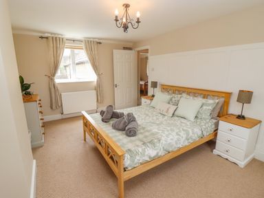 A bedroom with a bed a chest of drawers bedside tables and a window with curtains at The Cornerstone in Bourton-On-The-Water