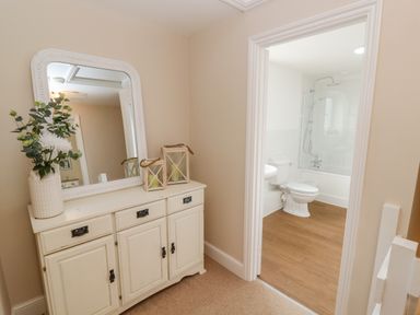 A hallway with a white cabinet and a mirror next to a bathroom with a toilet and bathtub at The Cornerstone in Bourton-On-The-Water
