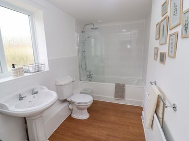 A bathroom with a pedestal sink a toilet a bathtub with shower and framed pictures on the wall at The Cornerstone in Bourton-On-The-Water