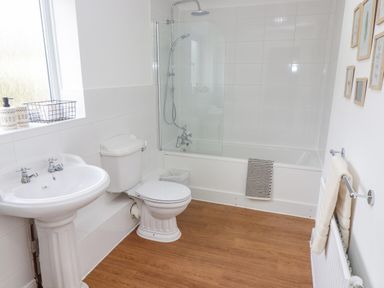A bathroom with a sink toilet bathtub with shower screen and wooden floor at The Cornerstone in Bourton-On-The-Water