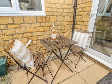 A small outdoor patio with a wooden table and two chairs with striped cushions at The Cornerstone in Bourton-On-The-Water