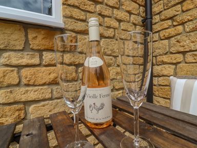 A bottle of wine and two empty wine glasses on a wooden table outside against a stone wall at The Cornerstone in Bourton-On-The-Water