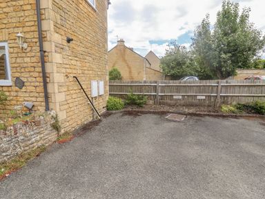 A parking space beside a stone building with a wooden fence and trees at The Cornerstone in Bourton-On-The-Water