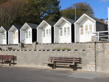 A row of beach huts behind a stone wall with benches in front at The Cottage in Wimborne Minster