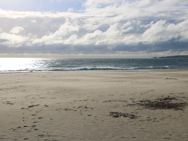 A sandy beach with footprints and the ocean under a cloudy sky at The Cottage in Wimborne Minster