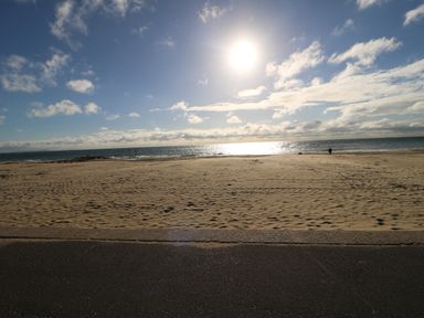 A sandy beach with ocean water and a person walking near the shore under a sunny sky at The Cottage in Wimborne Minster