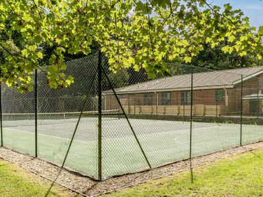 A tennis court enclosed by a fence with a building in the background at The Cottage in Wimborne Minster
