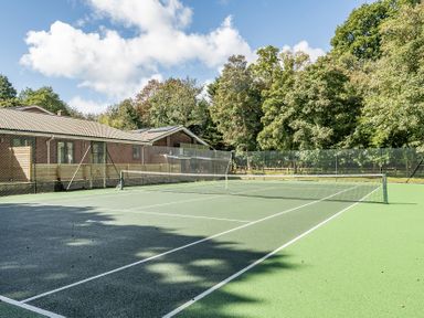 A tennis court with a net and surrounding fence at The Cottage in Wimborne Minster
