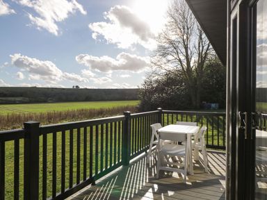 An outdoor deck with a white table and four chairs overlooking a grassy field at Manor Farm Lodge in Bowerchalke