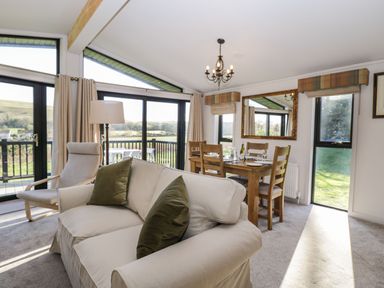 A living room with a sofa and armchair next to a dining table with chairs and a large mirror at Manor Farm Lodge in Bowerchalke