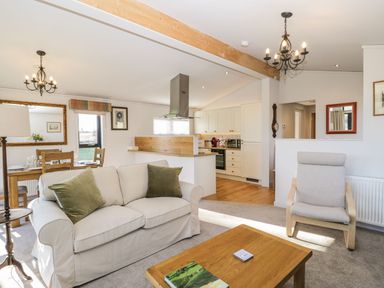 A living room with a sofa and armchair next to an open kitchen and dining area at Manor Farm Lodge in Bowerchalke