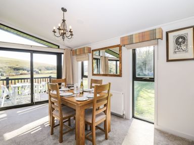 A dining room with a wooden table and chairs next to large sliding glass doors at Manor Farm Lodge in Bowerchalke