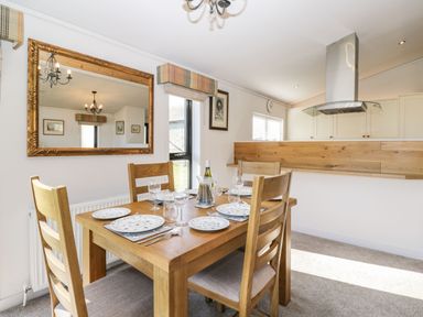 A dining area with a wooden table set with plates glasses and cutlery and four wooden chairs near a large wall mirror at Manor Farm Lodge in Bowerchalke