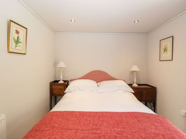 A bedroom with a double bed with red checkered headboard red blanket white pillows wooden bedside tables and lamps at Manor Farm Lodge in Bowerchalke