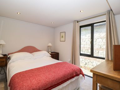 A bedroom with a double bed with a red blanket bedside tables with lamps a framed picture window with curtains and a wooden desk at Manor Farm Lodge in Bowerchalke