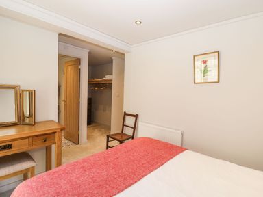 A bedroom with a wooden dressing table and chair a bed with a red blanket an open door leading to a walk-in closet at Manor Farm Lodge in Bowerchalke
