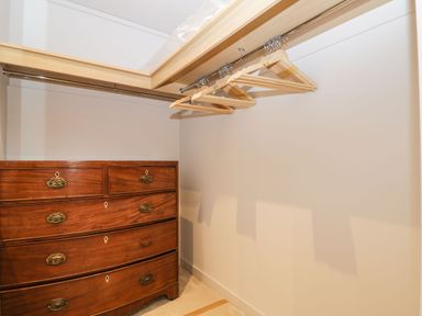 A walk in closet with wooden hangers on a rod and a wooden chest of drawers at Manor Farm Lodge in Bowerchalke