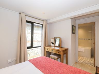 A bedroom with a wooden dressing table and mirrors by a window with beige curtains and an open door leading to a bathroom at Manor Farm Lodge in Bowerchalke