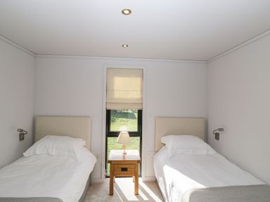 A bedroom with two single beds and a wooden bedside table with a lamp at Manor Farm Lodge in Bowerchalke